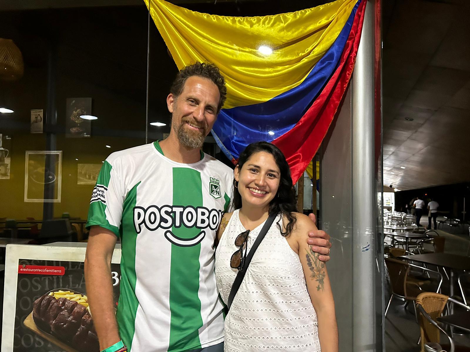 Dave Kramer and Alejandra Cano stand in front of a restaurant with a Colombian flag in the window.