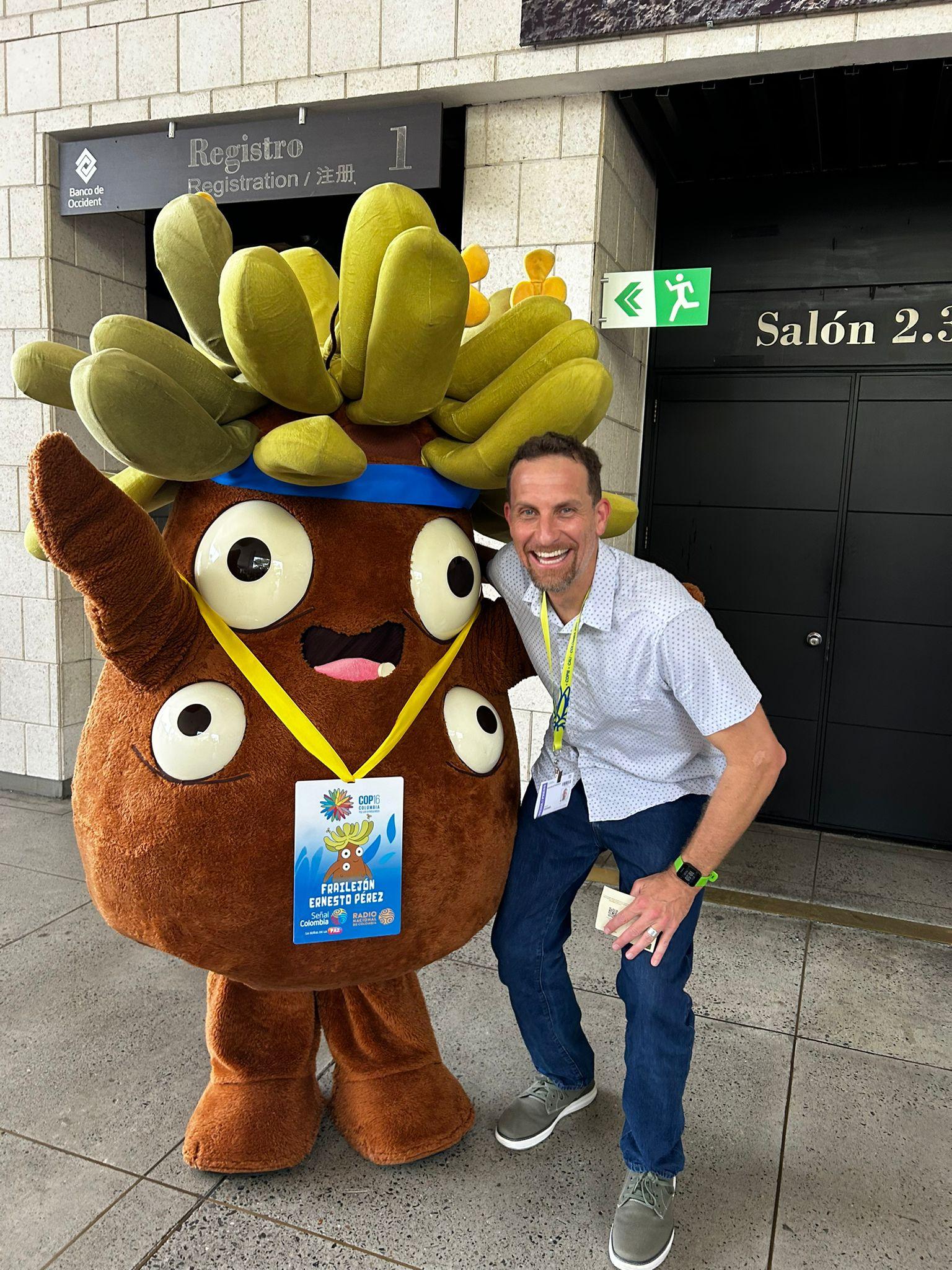 Dave crouches next to a mascot of Ernesto Perez el Frailejón at COP16.