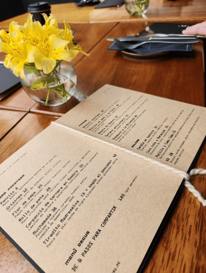 CCORI’s Cocina Óptima menu sits on a brown wooden table with a vase of yellow flowers